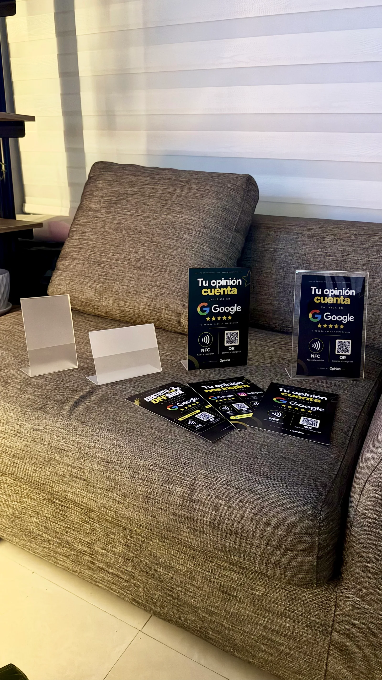 Soportes reales de OPINION sobre un sofá: soportes transparentes, soportes negros con NFC y QR para reseñas de Google y tarjetas